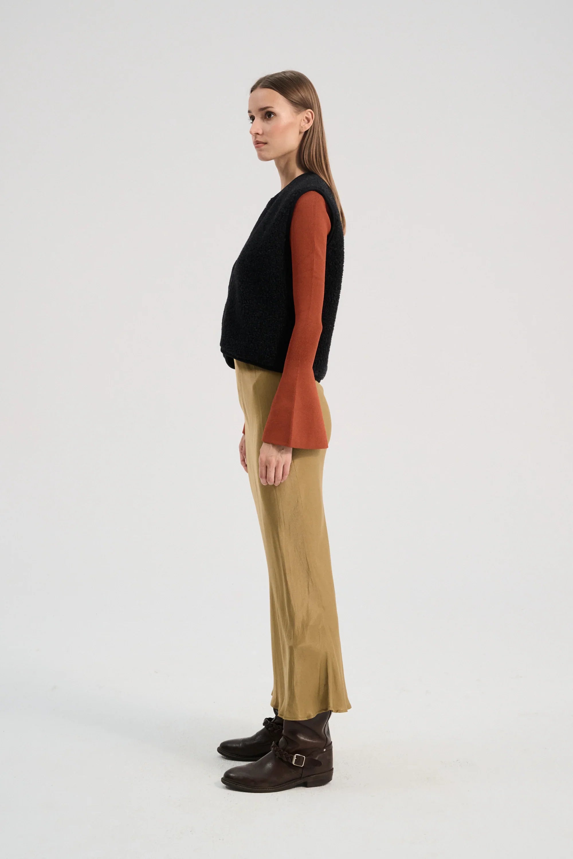 Woman wearing a black wool sweater, rust-colored shirt, beige pants, and brown boots on a white background