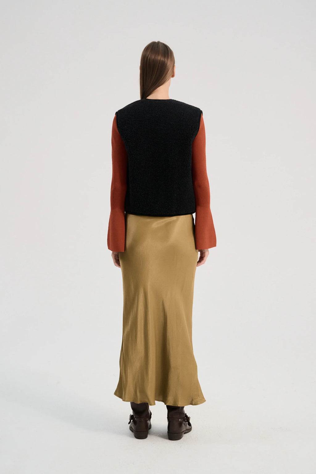 Person wearing a black vest, red long-sleeve shirt, and beige skirt on a white background