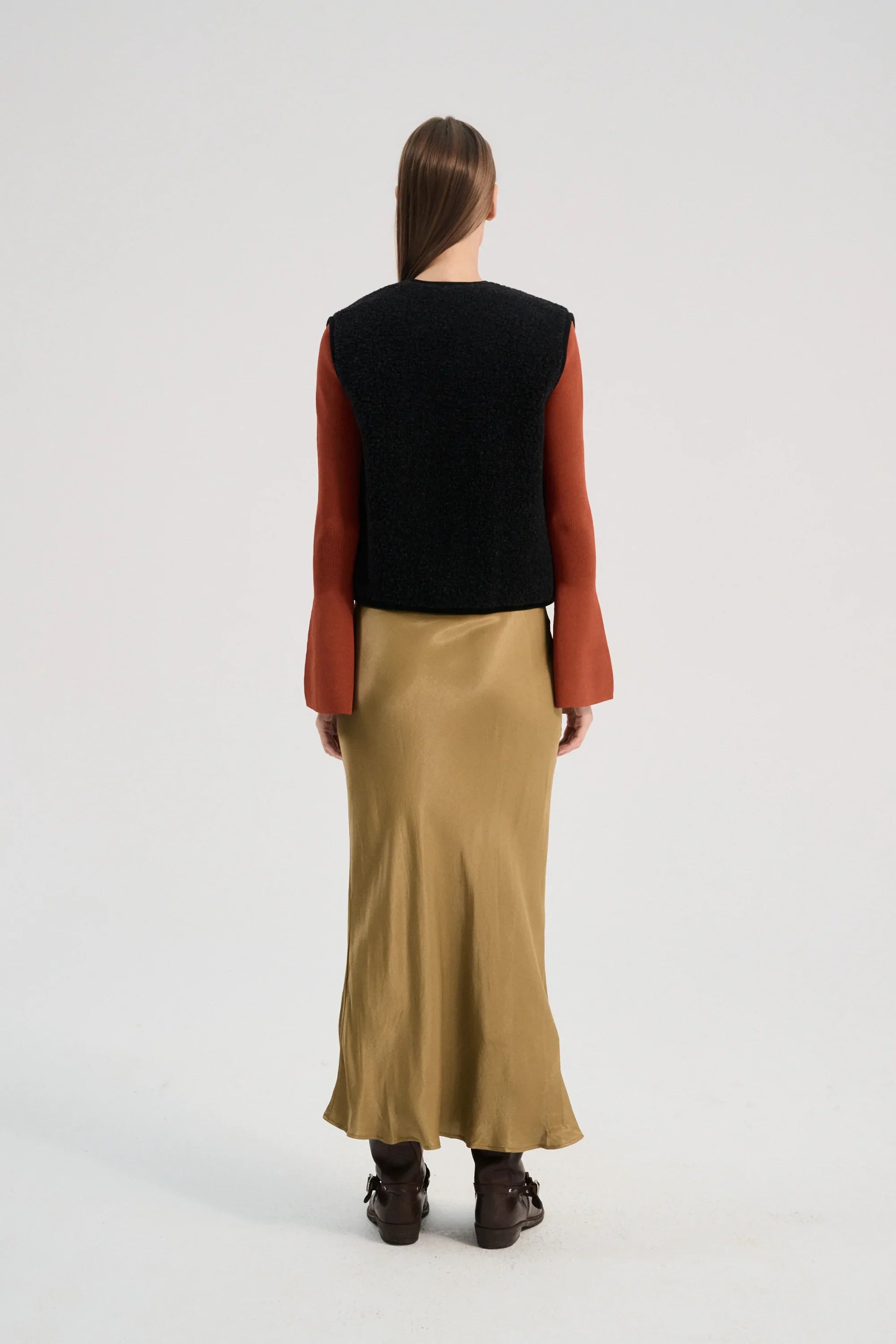 Person wearing a black vest, red long-sleeve shirt, and beige skirt on a white background