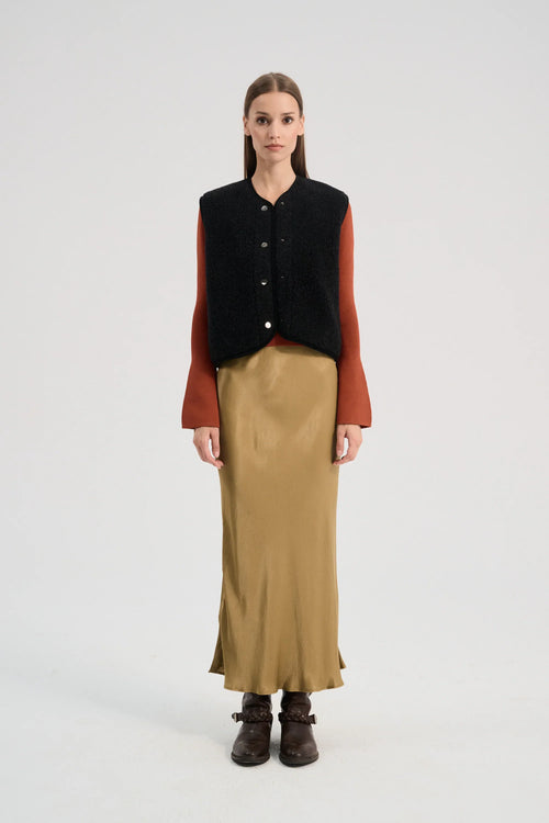 Woman wearing a black vest over a rust-colored shirt with a beige skirt on a white background